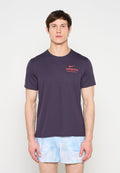 Mann trägt ein dunkelviolettes Nike London T-Shirt und hellblaue Shorts, steht vor einem schlichten weißen Hintergrund.