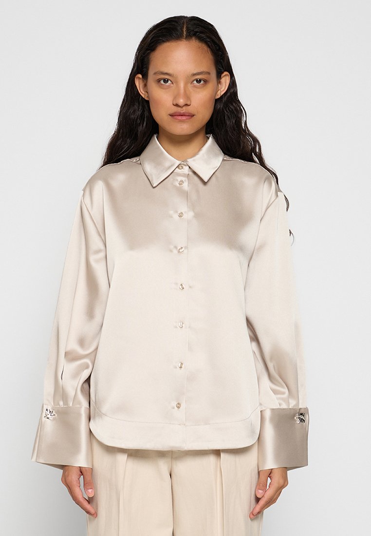 Beige Satin-Hemd mit Knöpfen, Kragen, langen Ärmeln und großen Manschetten mit dekorativer Hardware. Glatte Textur und lockere Passform.