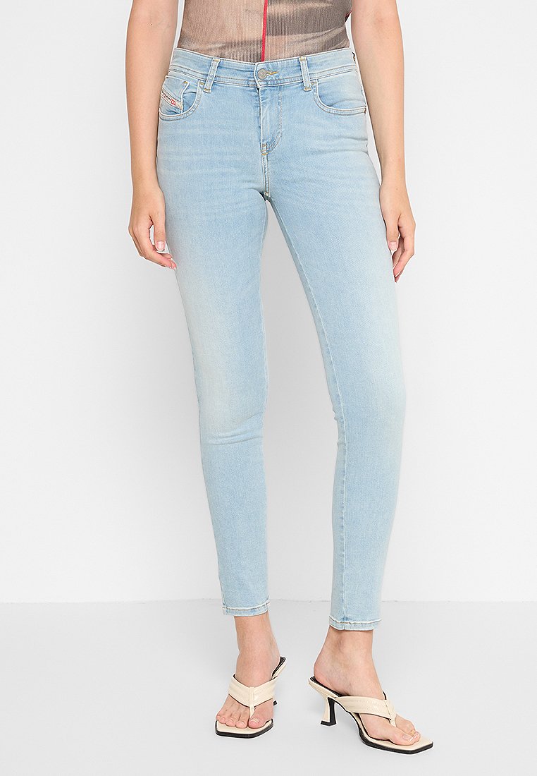 Hellblaue Skinny-Jeans mit glattem Denim-Textur, fünf Taschen, dezentem Verblassen und einem Reißverschluss. Getragen mit hellfarbigen Absatzsandalen.