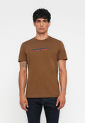 Mann mit dunklen Haaren trägt ein braunes T-Shirt von Diesel Industry Denim Division und dunkle Jeans, steht vor einem schlichten weißen Hintergrund.