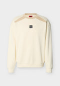 Cremefarbener Langarm-Sweatshirt mit beigen Schulterakzenten und einem kleinen schwarzen quadratischen Logo-Patch in der Mitte der Brust.