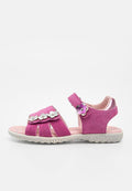 Rosa Kindersandale mit floralen Ausschnitten, silbernen und lila Blumenverzierungen sowie einem Klettverschluss am Knöchelriemen auf einer strukturierten weißen Sohle.