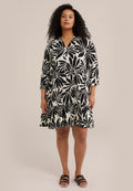 Schwarz-weißes Kleid mit Blattformen, V-Ausschnitt, dreiviertel Ärmeln und schichtweise Rock. Kombiniert mit schwarzen Sandalen.