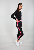 Schwarzes, kurzes Sweatshirt und schwarze Leggings mit rotem "REMOVE BEFORE FLIGHT"-Text auf dem Bund und seitlichem Streifen. Weiße Sneaker.