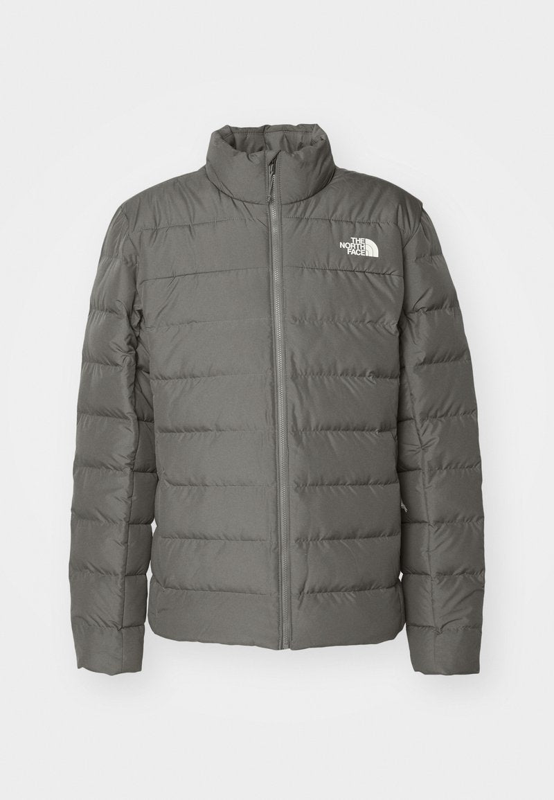Graue Pufferjacke mit hohem Kragen, horizontal genähten Bereichen, einem Reißverschluss vorne und einem Logo in der oberen linken Ecke.