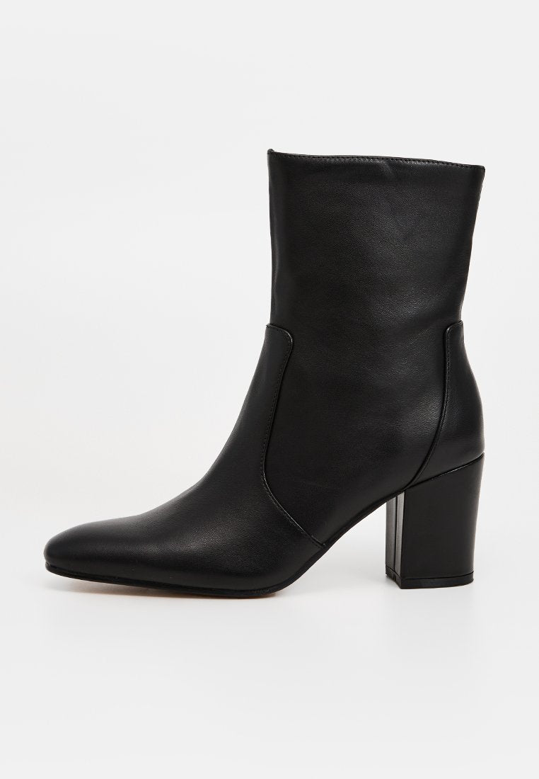 Schwarzer Stiefel bis zum Knöchel aus glattem Leder, mit spitzer Zehenpartie und klobigem Blockabsatz. Das Design ist schlank und ohne sichtbare Beschläge.