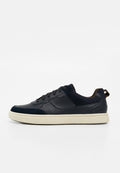 Schwarzer flacher Ledersneaker mit schwarzen Schnürsenkeln und beiger Gummisohle auf weißem Hintergrund, Seitenansicht des linken Schuhs.