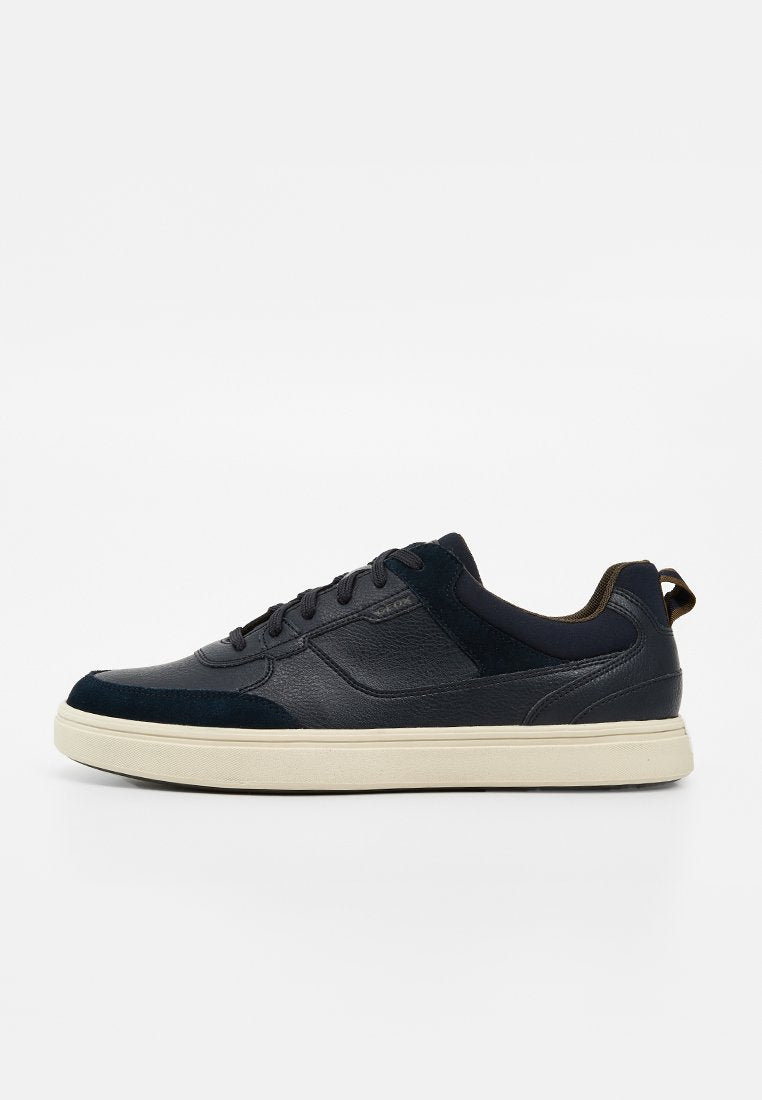 Schwarzer flacher Ledersneaker mit schwarzen Schnürsenkeln und beiger Gummisohle auf weißem Hintergrund, Seitenansicht des linken Schuhs.