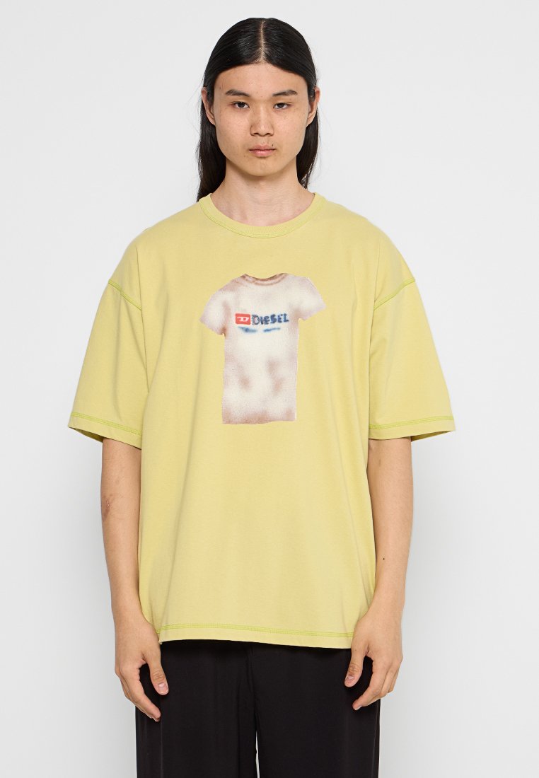 Gelbes, übergroßes T-Shirt mit einem grafischen Print eines weißen T-Shirts. Hat kurze Ärmel und kontrastierende Nähte.