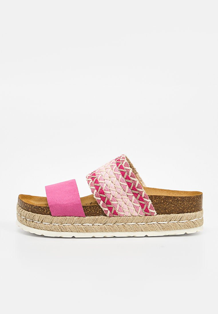 Flache Sandale mit Korksohle, rosa Wildleder-Vorderriemen und breitem geflochtenem Riemen in verschiedenen Rosatönen und Beige vor weißem Hintergrund.