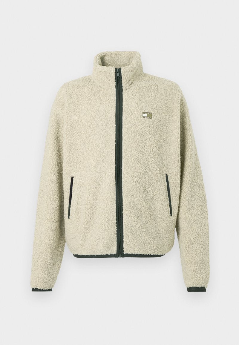 Beige Sherpa-Fleece-Jacke mit schwarzem Reißverschluss und Taschenbesatz, hohem Kragen, langen Ärmeln und einem kleinen rechteckigen Logo auf der Brust.