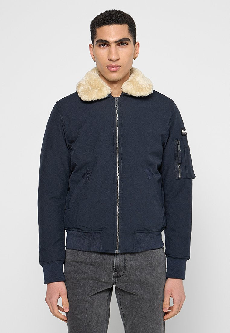 Marineblaue Bomberjacke mit Kunstfellkragen, Frontreißverschluss, seitlichen Taschen und gerippten Bündchen. Verfügt über eine zusätzliche Tasche am Ärmel.