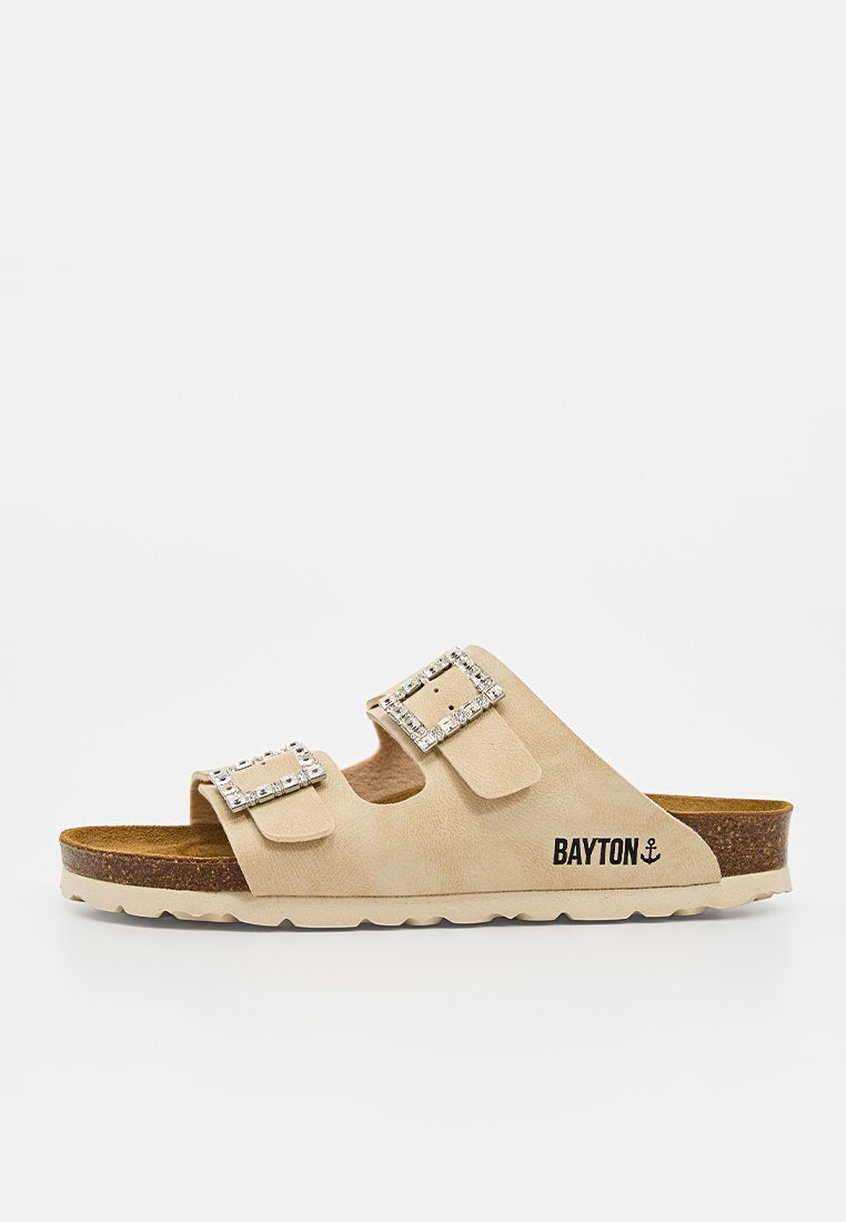 Beige Slide-Sandale mit zwei verstellbaren Schnallen, besetzt mit Strasssteinen und einem Korkfußbett, beschriftet mit BAYTON und einem Ankersymbol.