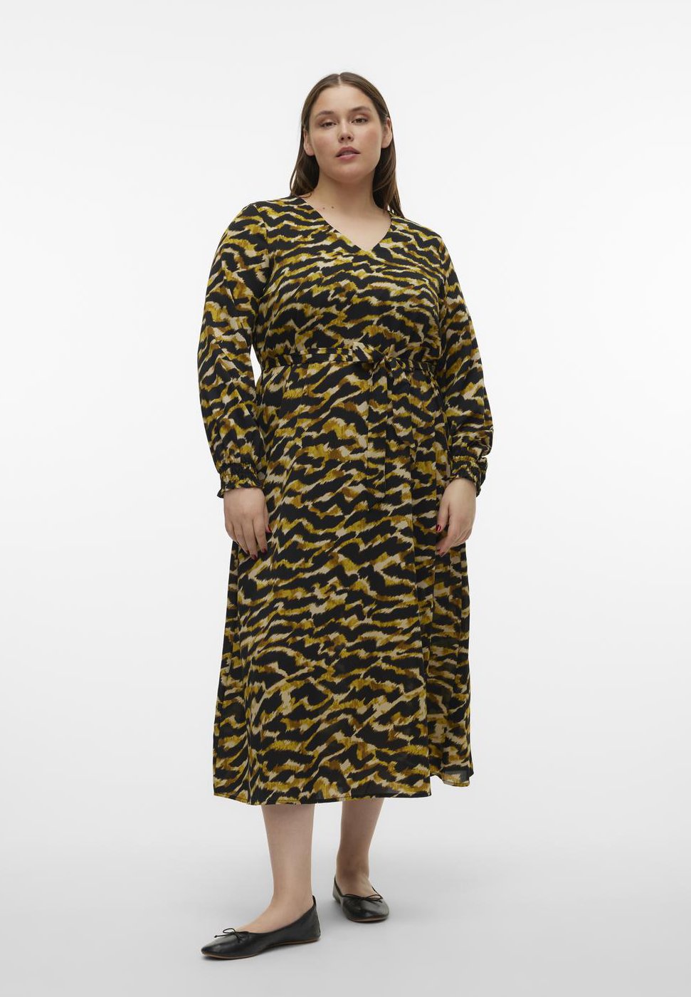 Langes Kleid in einem Schwarz-, Gelb- und Braun-Tierdruck, mit Wickeldesign, langen Ärmeln und einem Bindegürtel in der Taille. Flache Schuhe getragen.