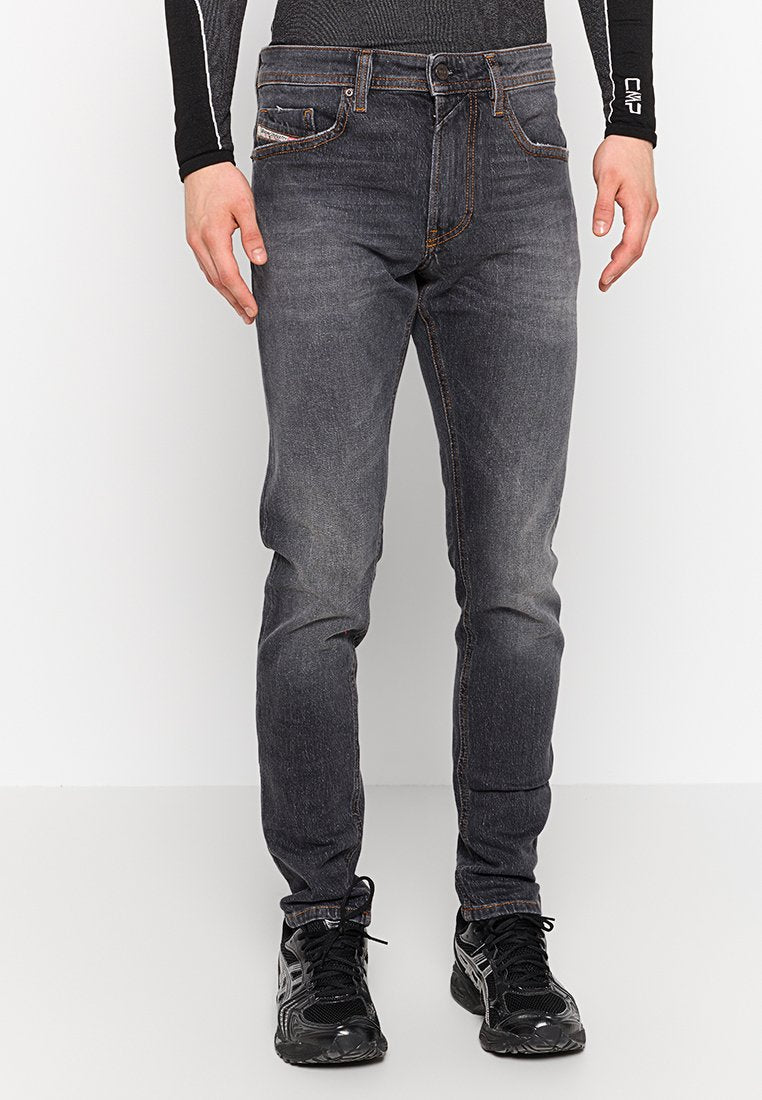 Schlanke, dunkelgraue Denim-Jeans mit subtilen Ausbleichungen, Fünf-Taschen-Design und Kontrastnähten, kombiniert mit schwarzen Sportschuhen.