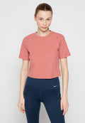 Junge Frau mit zurückgebundenem Haar, die ein kurzärmliges pinkes Crop-Top und navyblaue hoch geschnittene Sportleggings trägt.
