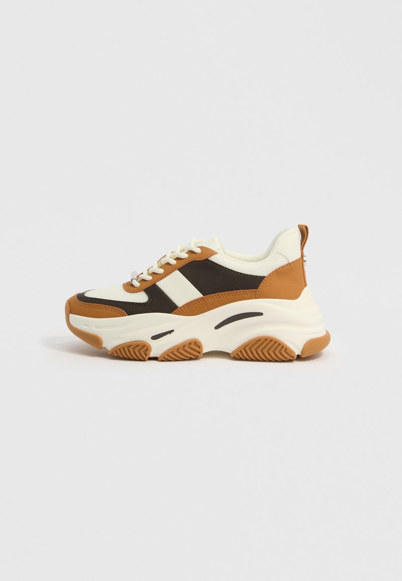 Klobiger Sneaker in Creme, Braun und Schwarz. Verfügt über ein strukturiertes Obermaterial, eine dicke Sohle und Gummidetails. Schnürdesign mit minimalem Branding.