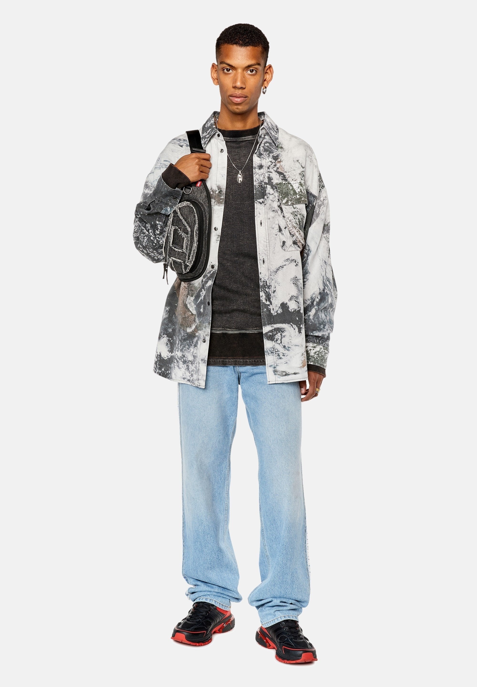 Baumwollhemd mit einem grauen und weißen abstrakten Muster, über einem schwarzen Pullover geschichtet. Blaue Jeans und schwarze Sneakers mit roten Akzenten.