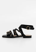 Schwarze flache Sandalen mit mehreren Riemen, die mit metallischen Schnallen und Ringen versehen sind. Hergestellt aus glattem Material, mit offener Zehenpartie und einem flachen Profilsohle.