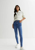 Weißes Button-up-Hemd, helle, hochtaillierte Skinny-Jeans und weiße Sneaker. Das Outfit zeichnet sich durch einen lässigen, taillierten Stil aus.