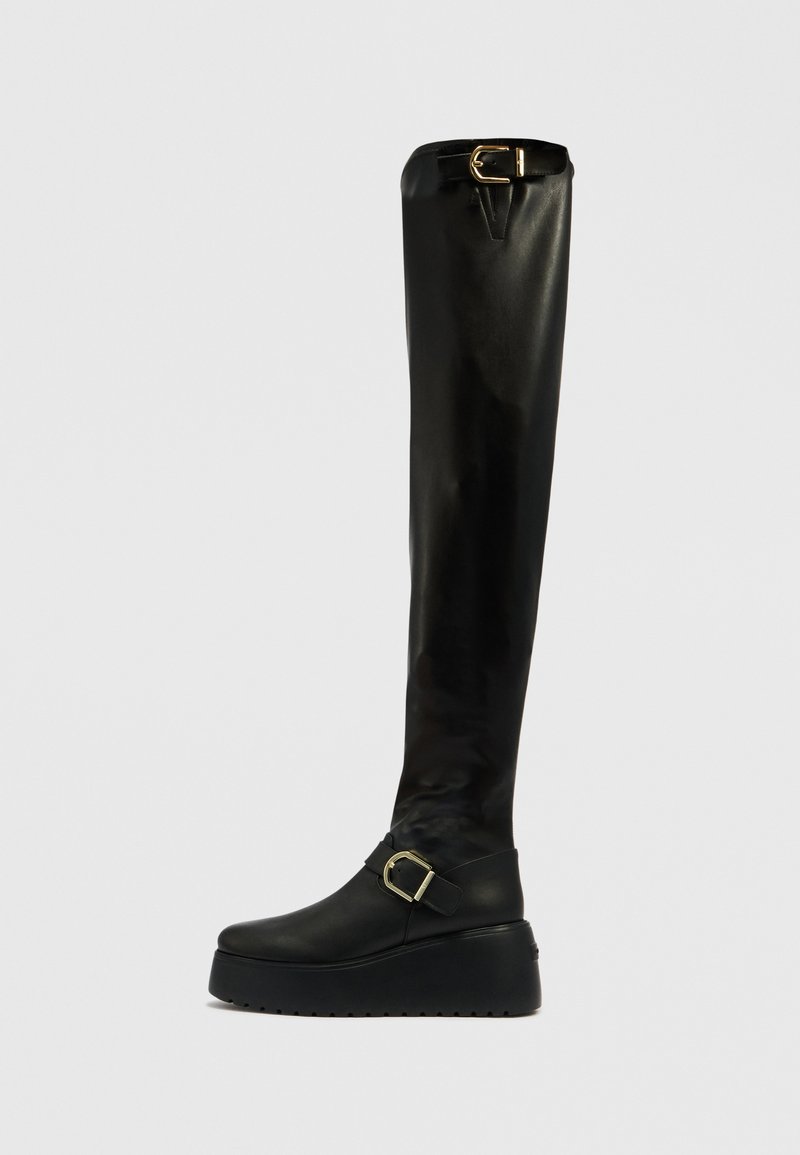 Schwarze Overknee-Stiefel mit glatter Oberfläche, ausgestattet mit einem goldenen Schnallendetail am Knöchel und einer dicken Plateau-Sohle.