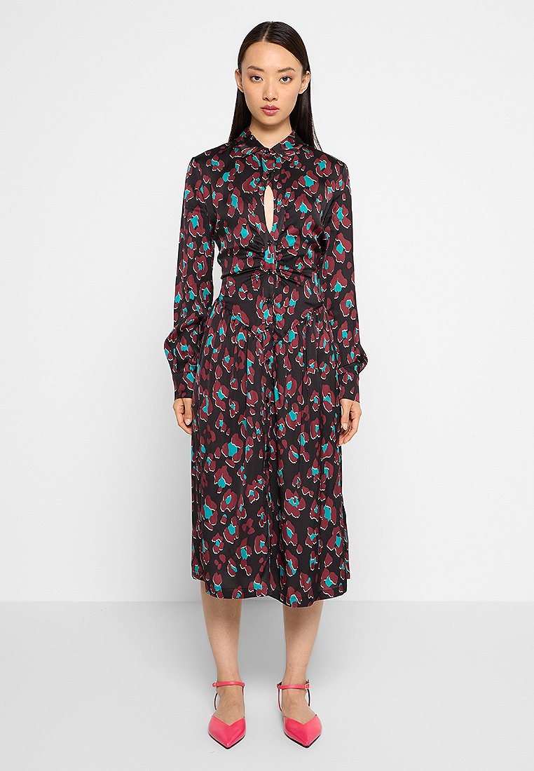 Schwarzes Kleid mit langen Ärmeln, knöpfbarem Kragen und einem Ausschnitt-Detail. Verfügt über einen bunten Blumenmuster in Türkis und Burgunderrot. Mittellang und fließend.