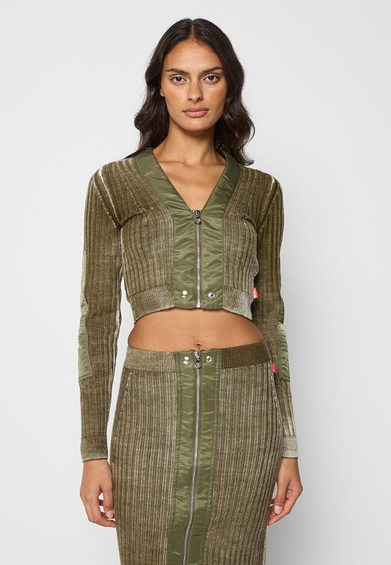 Olivgrüne verkürzte Jacke mit gerippter Textur, Reißverschluss und Satinakzenten, kombiniert mit einem passenden Rock mit vertikalen Paneelen und Reißverschlüssen.