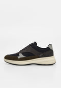Low-Top Sneaker mit schwarzem Stoff, dunkelgrauen und olivgrünen Wildledereinsätzen, beiger Sohle und schwarzen Schnürsenkeln auf weißem Hintergrund.