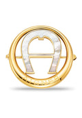 Goldfarbener Brosche mit einem runden Design, das ein perlisiertes "A"-Detail und den eingravierten Markennamen aufweist; glatte Metalloberfläche mit polierter Textur.