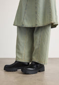 Schwarze Knöchelstiefel mit massiven, strukturierten Sohlen kombiniert mit weiten, hellgrünen Jeanshosen mit kontrastierenden Nähten.