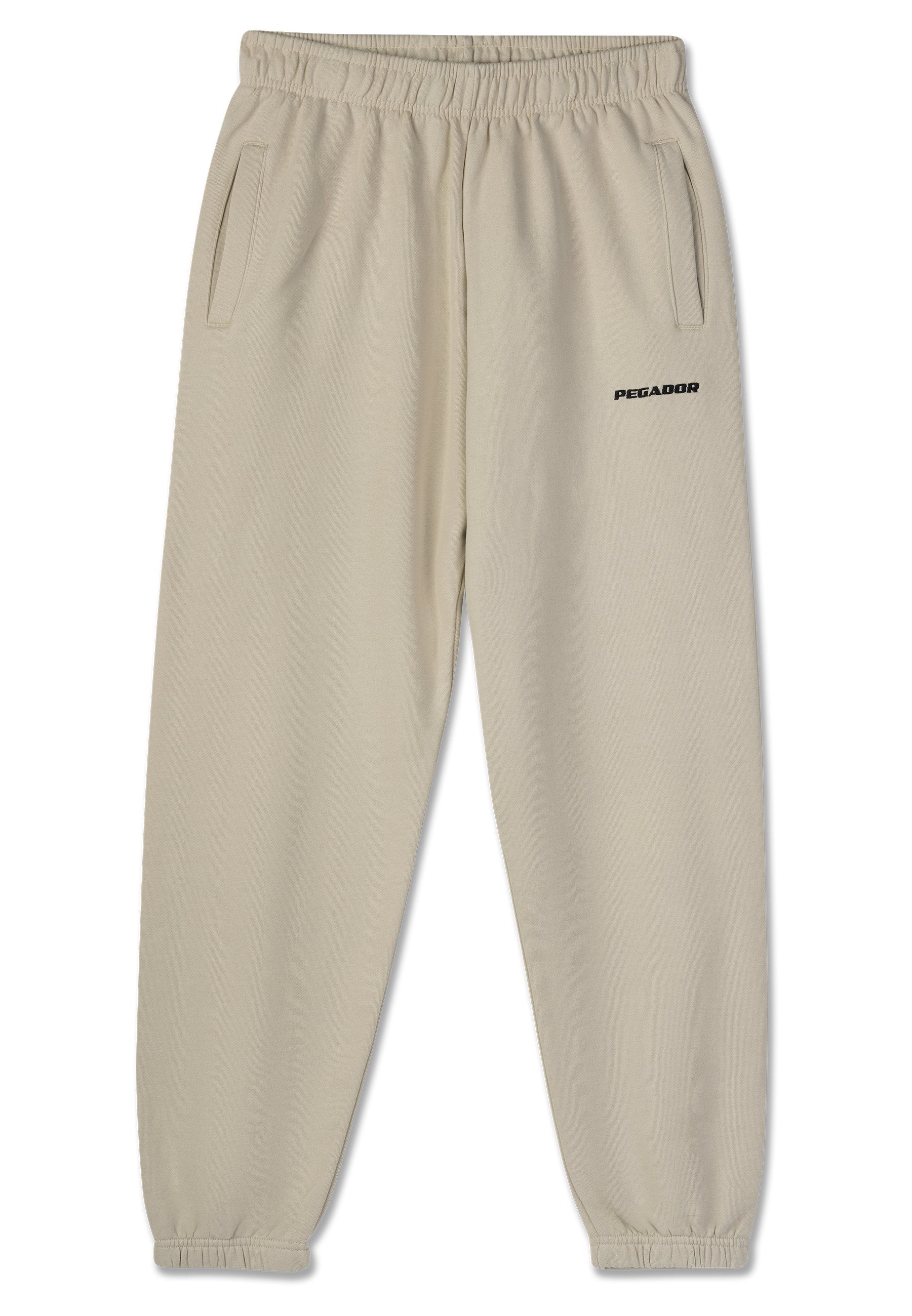 Beige Jogginghose mit einem elastischen Bund, zwei Seitentaschen und einem schwarzen "PEGADOR"-Logo, das auf dem linken Bein aufgedruckt ist. Glatte Stoffoberfläche.