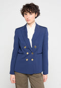 Marineblaues, doppelt verblasenes Blazer mit goldenen Knöpfen, scharfen Revers und zwei Seitentaschen, kombiniert mit einer weißen Bluse. Strukturierter Stoff.