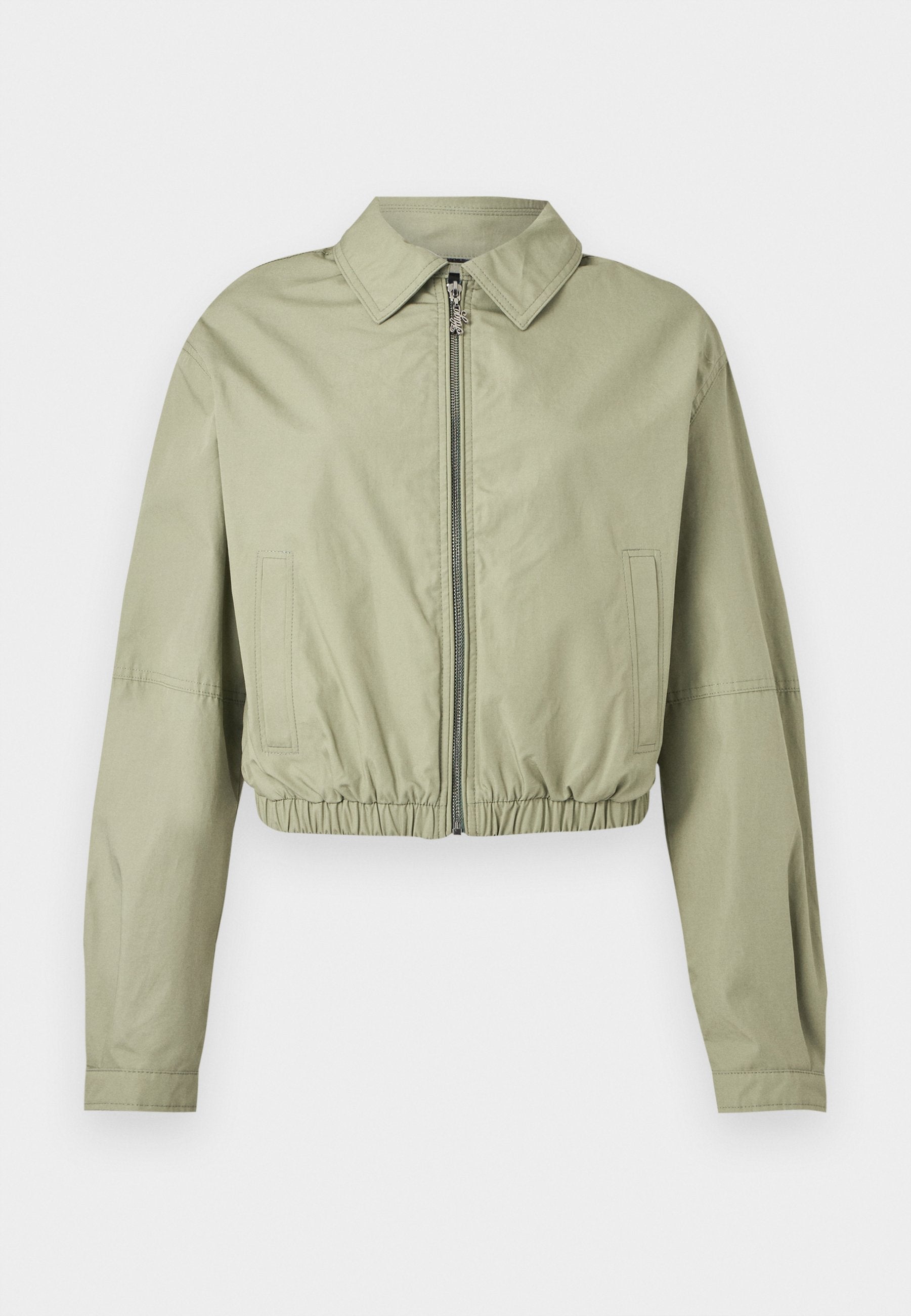 Hellgrüne, kurze Jacke mit langen Ärmeln, spitzem Kragen, Frontreißverschluss, seitlichen Taschen und elastischem, gerafftem Taillenbund vor weißem Hintergrund.