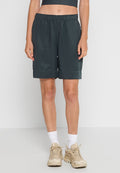 Person mit schwarzen elastischen Shorts, weißen Crew-Socken, beigen klobigen Sneakern und einem dunklen, kurzen Oberteil, das vor einem weißen Hintergrund steht.