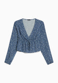 Blaues Blusenoberteil mit langen Ärmeln, tiefem V-Ausschnitt, geraffter Taille und einem Peplum-Saum. Verfügt über kleine, weiße Blumenmuster auf einem strukturierten Stoff.
