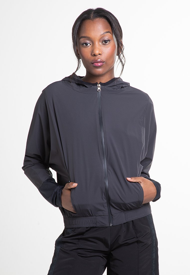 Schwarze leichte Jacke mit Kapuze, vorderem Reißverschluss und elastischen Bündchen. Verfügt über seitliche Taschen und eine glatte, matte Textur.
