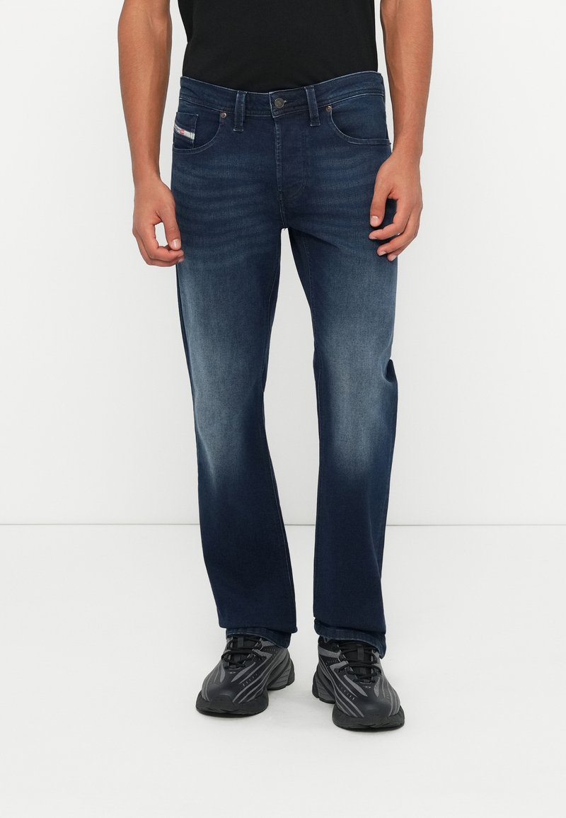 Dunkelblaue Jeans mit geradem Bein, dezentem Ausbleichen und einem Design mit fünf Taschen. Kombiniert mit schwarzen Sportschuhen.