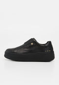 Schwarzer Leder-Sneaker in niedriger Ausführung mit dicker Sohle, Schlupfdesign, kleinem goldfarbenem Logoknopf und goldenem Schriftzug an der Fersenseite.