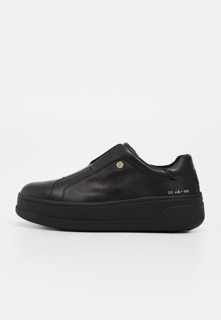 Schwarzer Leder-Sneaker in niedriger Ausführung mit dicker Sohle, Schlupfdesign, kleinem goldfarbenem Logoknopf und goldenem Schriftzug an der Fersenseite.