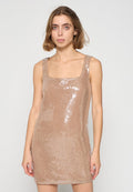 Junge Frau trägt ein ärmelloses, glitzerndes, beiges Mini-Kleid mit quadratischem Ausschnitt und steht vor einem schlichten hellgrauen Hintergrund.