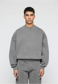 Mann, der nach vorne schaut und einen lockeren grauen Pullover sowie passende graue Hosen vor einem schlichten hellen Hintergrund trägt.