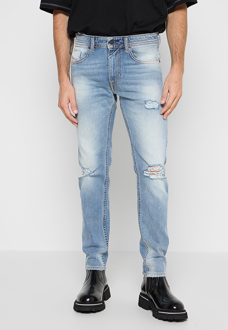 Helle blaue Jeans mit abgeriebenen Details, schmaler Schnitt und Fünf-Taschen-Design. Getragen mit schwarzen Chelsea-Stiefeln mit dicker Sohle.