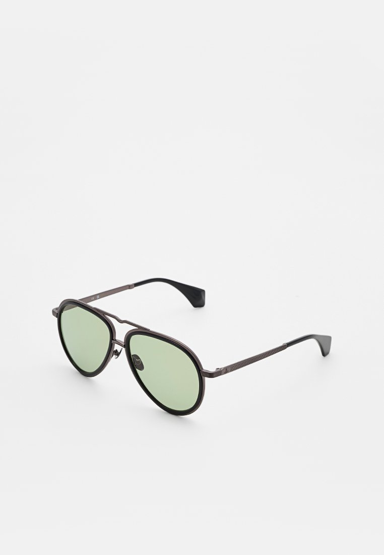 Sonnenbrille mit Metallrahmen und grünen Gläsern. Runde Form, dünne Augenbraue, strukturierte Bügel und schwarze Akzente. Minimalistisches Design, leicht.