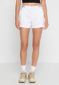 Frau, die weiße Sportshorts mit seitlichen Taschen, beigen Sneakern, weißen Socken und einem schwarzen Cropped-Top trägt, steht vor einem schlichten Hintergrund.