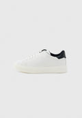 Weißer Sneaker mit niedrigem Schaft, weißen Schnürsenkeln, dicker Sohle und schwarzem Fersenkragen, im Profil vor hellem grauem Hintergrund gezeigt.