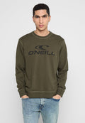 Junger Mann, der einen olivgrünen O'Neill-Sweatshirt und hellblaue Jeans trägt, steht mit den Händen in den Taschen vor einem schlichten Hintergrund.
