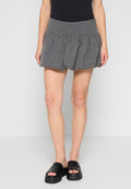 Grauer Skort mit gerafftem Bund und ausgestellter Form. Aus strukturiertem Stoff gefertigt, kombiniert mit schwarzen flachen Sandalen.