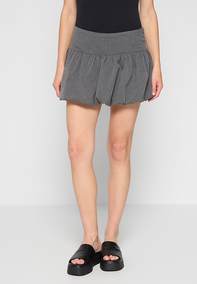 Grauer Skort mit gerafftem Bund und ausgestellter Form. Aus strukturiertem Stoff gefertigt, kombiniert mit schwarzen flachen Sandalen.