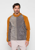 Mann trägt eine leichte Jacke mit orangen Ärmeln und grauem Körper, steht vor einem einfarbigen hellen Hintergrund.