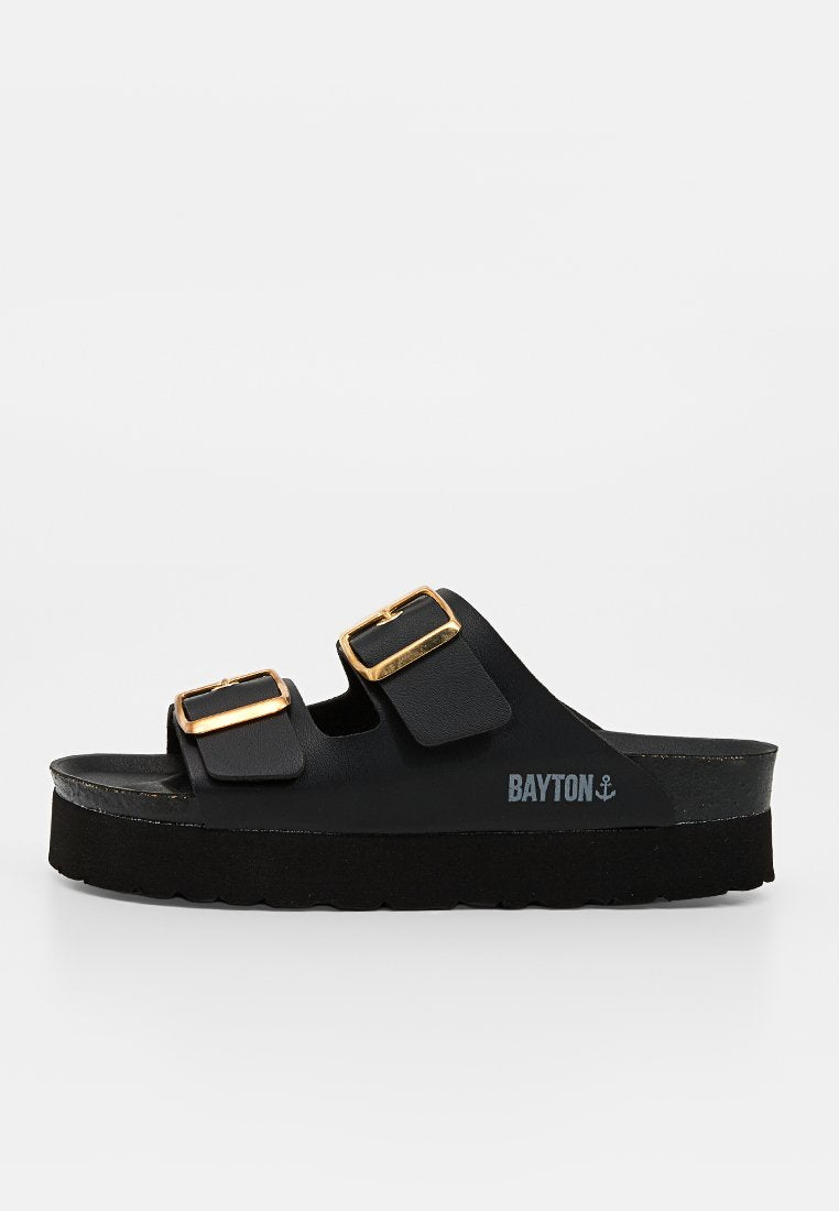 Schwarze Slip-On-Sandale mit zwei verstellbaren goldenen Schnallen und dicker Sohle, mit dem Markennamen Bayton und einem Ankerlogo an der Seite.